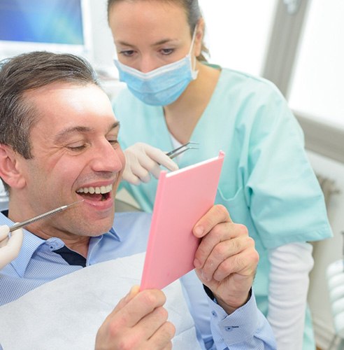 Man in dental chair smiling at result in mirror with dentist looking over his shoulder