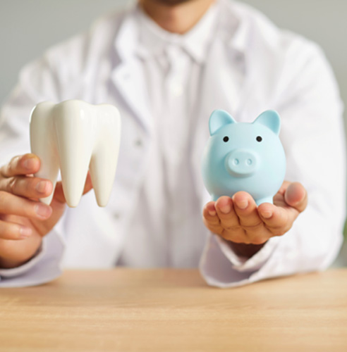 Dentist in white coat holding blue piggy bank and large model tooth