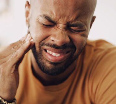 Man in tan shirt holding hand to jaw in pain