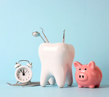  Pink piggy bank next to large tooth holding exam instruments next to white alarm clock