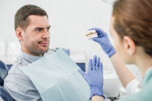 Dental patient with suspicious look while dentist explains something holding mold of mouth.